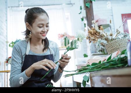 bonne jeune femme fleuriste portant un tablier vérifier l'état de la fleur Banque D'Images