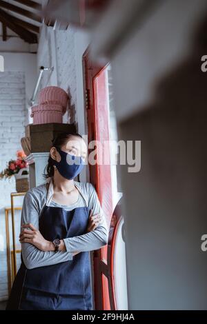 portrait femme ennuyeuse fleuriste portant un tablier et un masque de visage maigre sur la porte Banque D'Images