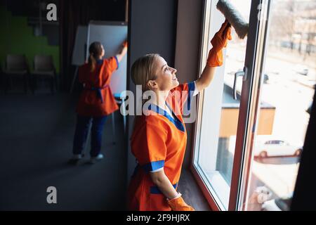 Une femme de ménage joyeuse et sa collègue qui fait le ménage Banque D'Images