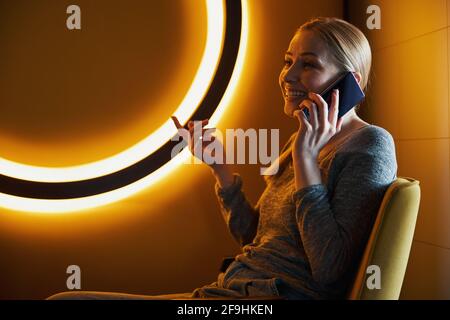 Merry lady assise dans le fauteuil parlant sur le smartphone Banque D'Images