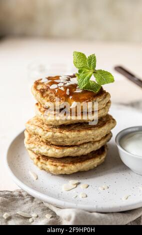 Une pile de crêpes végétariennes à l'avoine pour le petit-déjeuner, décorées de noix, de confiture et de menthe, sur fond de pierre légère. Mise au point sélective. Banque D'Images