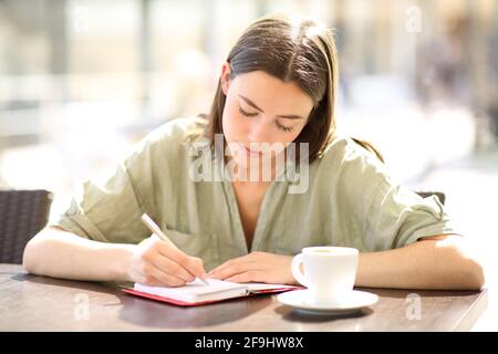 Portrait en vue de face d'une femme sérieuse écrivant à l'ordre du jour dans un café Banque D'Images