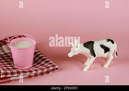 Figurine d'une vache jouet et d'un seau de lait sur fond rose. Un animal blanc avec des taches noires et un petit seau en métal plein de lait naturel. Rouge CH Banque D'Images