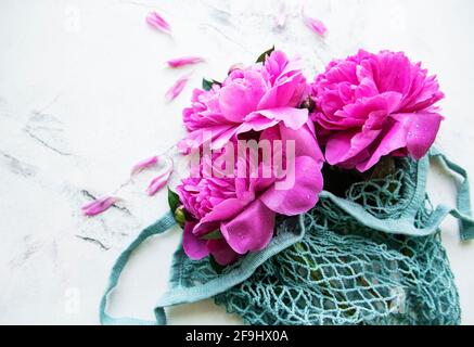 Magnifiques pivoines roses dans un sac à ficelle tendance sur fond de marbre blanc. Fond floral naturel. Banque D'Images