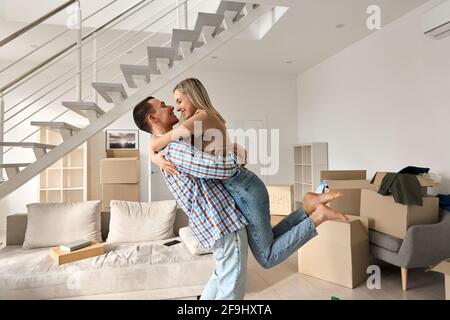 Un jeune couple heureux, propriétaires de la première fois, qui s'embrasse dans la salle de séjour lors d'une journée de déménagement. Banque D'Images