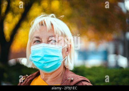 Femme blanche blonde adulte 50 ans en robe brillante et masque de protection respiratoire médical en regardant loin sur le parc Banque D'Images