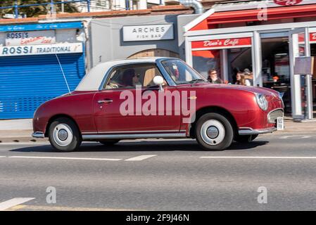 Nissan Figaro conduisant à Southend sur la mer, Essex, Royaume-Uni, lors d'une journée ensoleillée et lumineuse de printemps, En passant par le café Arches, restaurants. Couleur de corps magenta non standard Banque D'Images