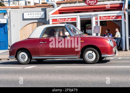 Nissan Figaro conduisant à Southend sur la mer, Essex, Royaume-Uni, lors d'une journée ensoleillée et lumineuse de printemps, En passant par le café Arches, restaurants. Couleur de corps magenta non standard Banque D'Images