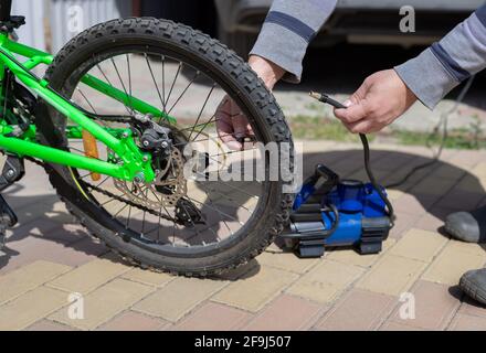 l'homme fait tourner le mamelon sur la roue de la bicyclette pour enfants, après avoir pompé un pneu crevé avec le compresseur Banque D'Images