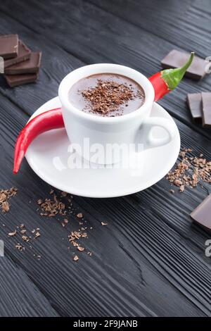 Chocolat chaud dans la tasse blanche et piment rouge sur fond de bois noir. Emplacement vertical. Banque D'Images