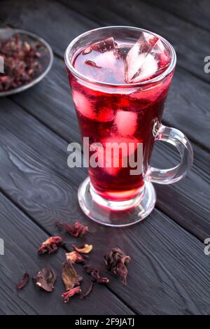 Thé glacé à l'hibiscus ou au karkade dans le verre sur fond de bois noir. Emplacement vertical. Gros plan. Banque D'Images