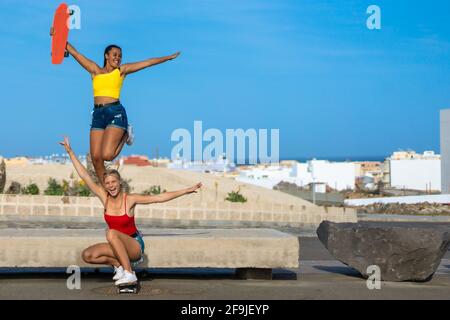 Deux amies jouant avec le skateboard dans la rue. Une fille sautant une autre fille patinant. Rire et plaisir. Banque D'Images