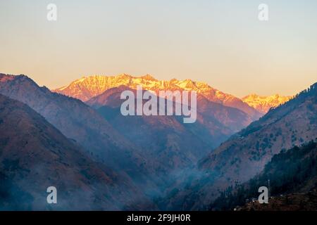 Des rayons de soleil au-dessus des sommets enneigés des montagnes, Pekhri, vallée de Tirthan, Himachal Pradesh, Inde Banque D'Images