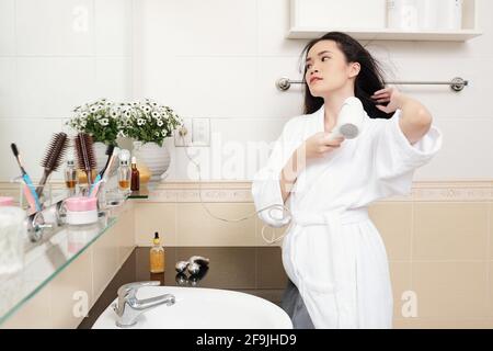 Belle élégante jeune femme asiatique soufflant ses cheveux après prendre une douche le matin Banque D'Images