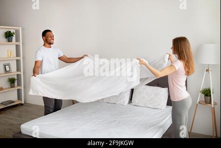 Couple multiracial gai faisant lit le matin, s'amuser à la maison Banque D'Images