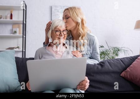 Une femme adulte embrasse une mère souriante avec un ordinateur portable sur un premier plan flou Banque D'Images