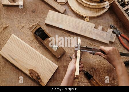 Mains de charpentier mesurant des planches en bois avec pied à coulisse, vue d'en haut Banque D'Images