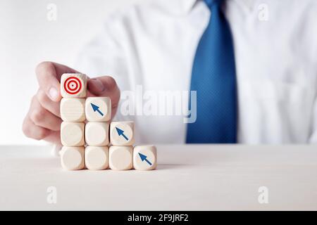 Définition d'objectifs ou d'objectifs ou réalisation d'objectifs dans l'entreprise. Homme d'affaires place un cube sur des cubes en bois à plusieurs niveaux avec des icônes de cible et de flèche. Banque D'Images