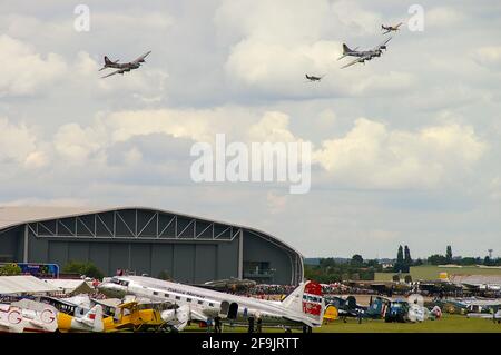 Un spectacle aérien au Musée impérial de la guerre, Duxford, Cambridgeshire, Royaume-Uni, avec deux bombardiers Boeing B-17 avec escorte de chasseurs survolant la foule et les avions Banque D'Images