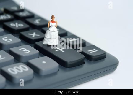 Robe de mariage budget pour mariée, miniature personnes illustration concept. Femme debout au-dessus de la calculatrice. Photo d'image Banque D'Images