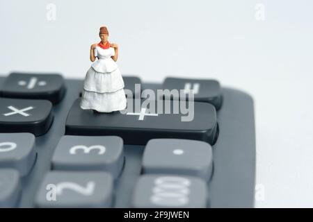 Robe de mariage budget pour mariée, miniature personnes illustration concept. Femme debout au-dessus de la calculatrice. Photo d'image Banque D'Images