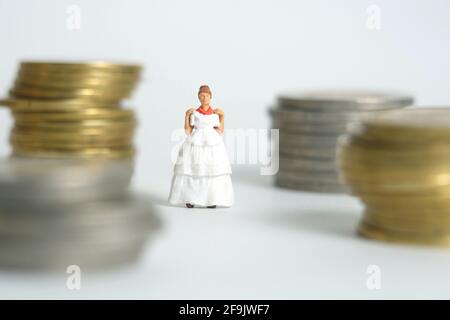 Robe de mariage budget pour mariée, miniature personnes illustration concept. Femme debout entre la pile de monnaie. Photo d'image Banque D'Images