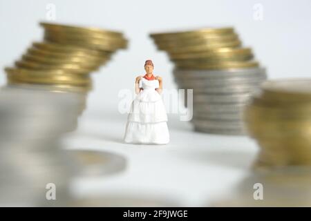 Robe de mariage budget pour mariée, miniature personnes illustration concept. Femme debout entre la pile de monnaie. Photo d'image Banque D'Images