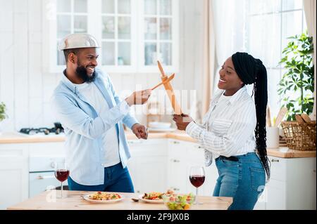 Les conjoints africains positifs se battent avec des ustensiles de cuisine tout en déjeunant Dans la cuisine Banque D'Images