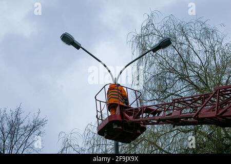 Un travailleur municipal en équipement de protection remplaçant les ampoules d'une lampe de rue. Un travailleur répare une lampe de rue d'un élévateur à godet. Banque D'Images