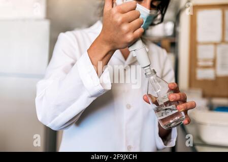 Photo de la scientifique féminine portant un masque facial remplissant des tubes à essai dans son laboratoire. Banque D'Images