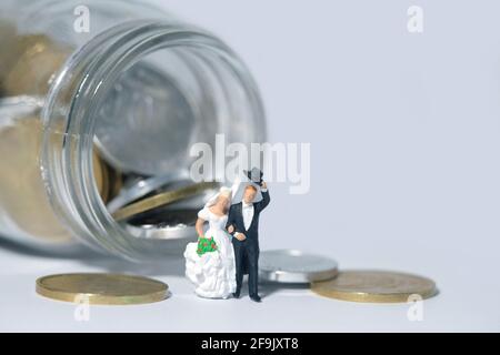 Mariage budget concept miniature personnes, jouets photographie. Mariée et marié avec de l'argent sur un verre de pot isolé sur fond blanc. Photo d'image Banque D'Images