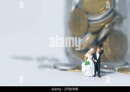 Mariage budget concept miniature personnes, jouets photographie. Mariée et marié avec de l'argent sur un verre de pot isolé sur fond blanc. Photo d'image Banque D'Images