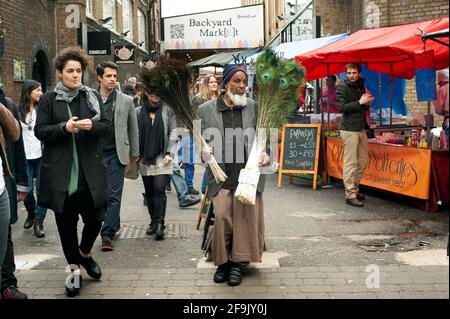 Homme musulman vendant des plumes de paon. Marché de rue du dimanche sur Brick Lane, East London, Royaume-Uni. AVR 2014 Banque D'Images