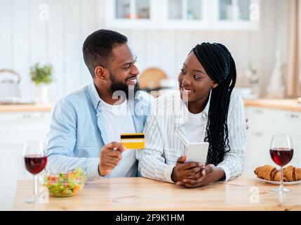 Black couple commande de nourriture en ligne avec un smartphone et une carte de crédit Dans la cuisine Banque D'Images