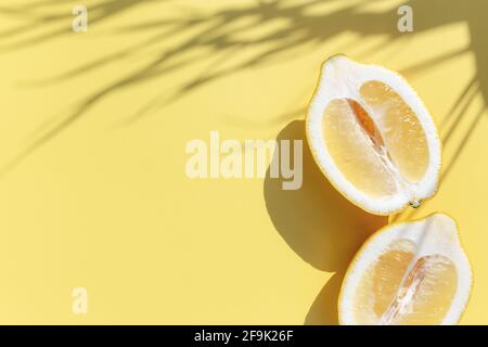 Deux coupes de citron coupées en deux avec ombre de la feuille de palmier sur fond jaune Banque D'Images