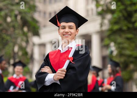 Joyeux jeune homme étudiant en costume de remise des diplômes montrant le diplôme Banque D'Images