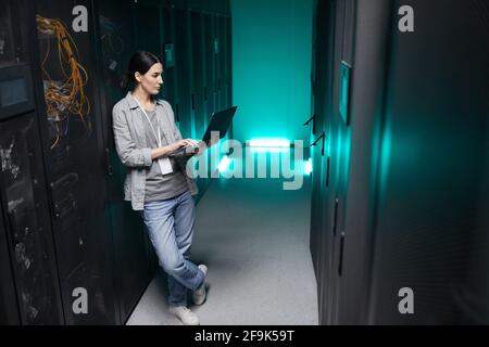 Portrait en grand angle complet d'une femme chargée de données, tenant un ordinateur portable tout en travaillant avec un superordinateur dans la salle des serveurs, espace de copie Banque D'Images