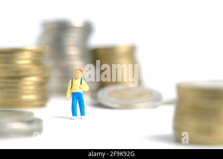 Budget d'admission à l'école. Un enfant, debout entre la pile de monnaie. Photo miniature de jouets de personnes minuscules. Isolé sur fond blanc. Banque D'Images