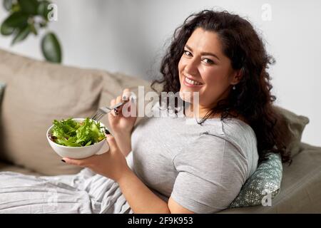 jeune femme souriante mangeant de la salade de légumes à la maison Banque D'Images