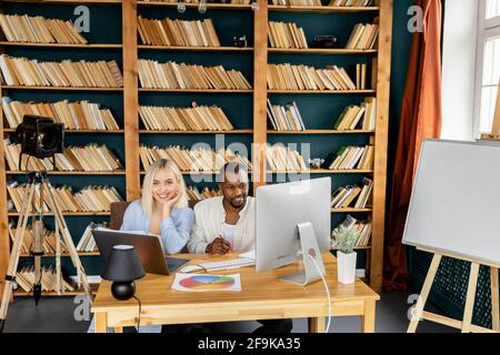 Des partenaires d'affaires heureux travaillant ensemble sur un projet au bureau, souriant, utilisant un ordinateur portable et un ordinateur. Collègues multiraciaux qui ont réussi à discuter de nouveaux Banque D'Images