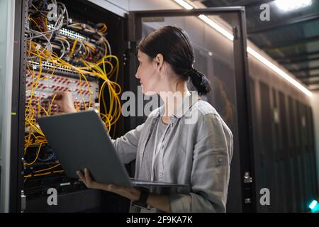 À la taille d'une femme ingénieur réseau qui connecte les câbles dans l'armoire de serveur tout en travaillant avec le superordinateur dans le centre de données, espace de copie Banque D'Images