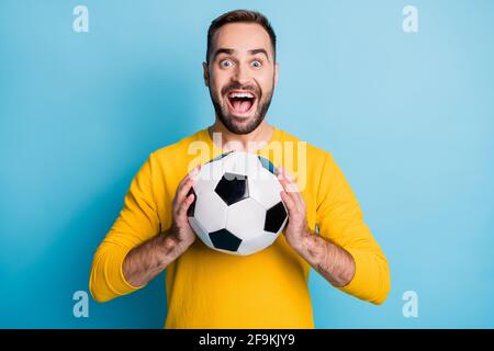 Photo de jeune excitée fou heureux positif souriant gai homme tenez le ballon de football dans les mains isolées sur fond bleu Banque D'Images