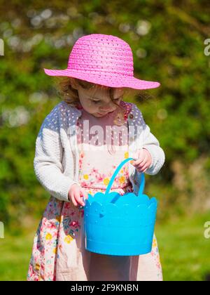 Petite fille sur une chasse aux oeufs de Pâques et les mettant dans un seau bleu, Royaume-Uni Banque D'Images