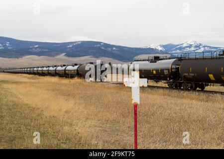 Une croix blanche marque un décès sur la route dans l'État du Montana. Derrière la croix se trouve une série de wagons-citernes stationnaires et inutilisés. Banque D'Images