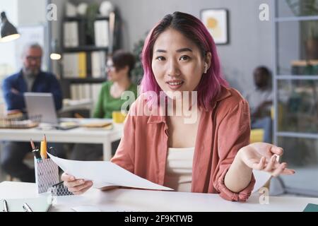 Portrait d'une jeune femme d'affaires asiatique regardant l'appareil photo pendant son travail à la table avec les documents au bureau Banque D'Images
