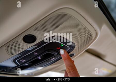 le doigt du conducteur de sexe féminin appuie sur le bouton sos du panneau de plafond d'une voiture moderne Banque D'Images
