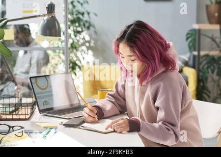 Jeune chinoise assise à la table et écrivant elle faire son travail pendant l'étude Banque D'Images