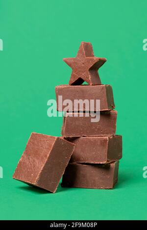 Morceaux de caramel au chocolat empilés sur une table verte. Tranches de fudge maison dans une pile isolée sur un fond coloré. Banque D'Images