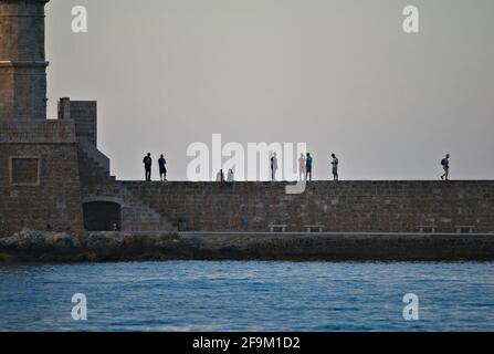 Coucher de soleil paysage avec des silhouettes de personnes sur le vieux phare au port vénitien de Chania en Crète, Grèce. Banque D'Images