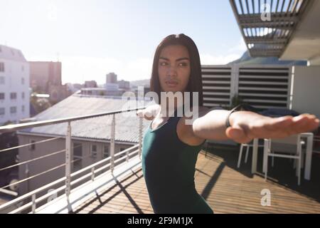 Femme transgenre de race mixte pratiquant le yoga debout sur la terrasse du toit au soleil Banque D'Images